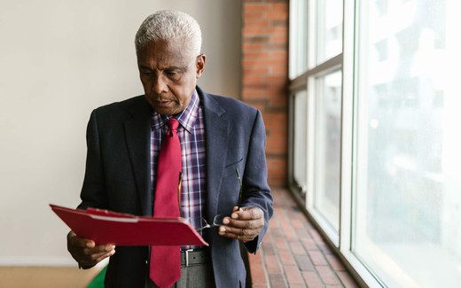 An executive reviews documents from a red folder while standing near a window