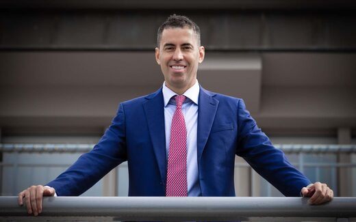 A smiling executive in a blue suit at an outdoor railing, a generic stand-in for Sumitomo Pharma America