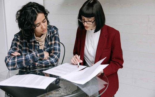 Two colleagues review a signed legal document together at a glass table, one holding a pen to the page