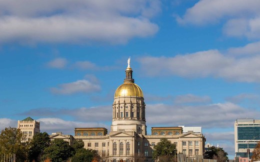 The gold dome of the Georgia State Capitol building rises against a partly cloudy blue sky