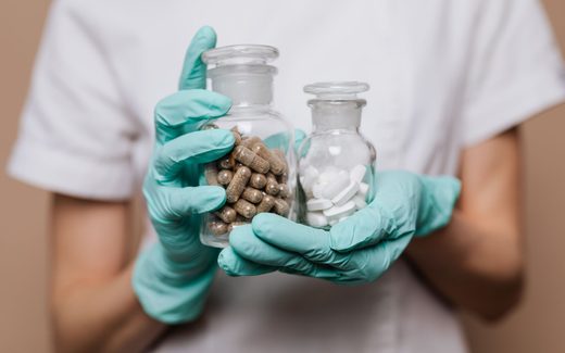Gloved hands hold two apothecary jars of capsules and tablets