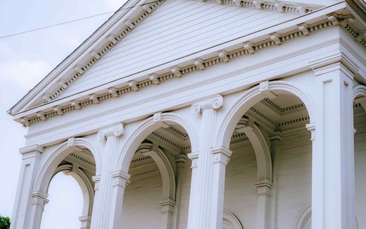 A close-up of a white neoclassical building's pediment and arched colonnade against a pale sky
