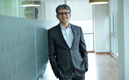 A confident executive in a gray suit stands in a bright glass-walled office corridor