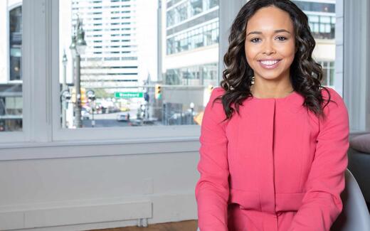 A smiling executive in a pink jacket at a city office window, standing in for SimBioSys's leadership announcing the TumorSight Risk clearance