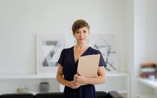 A confident executive holding a clipboard in a bright, minimal office, a generic stand-in for AstraZeneca leadership