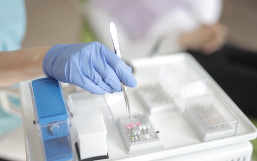 A gloved hand lifts forceps above a sterile surgical instrument tray