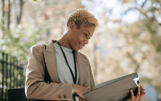 A professional reviews a folder of documents outdoors, lanyard and badge visible