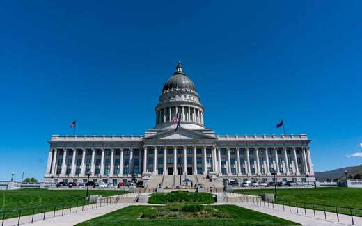 A domed state capitol building photographed from the lawn under a clear blue sky