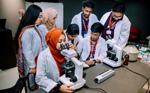 Two researchers in a bright teaching lab examine results together at a microscope station