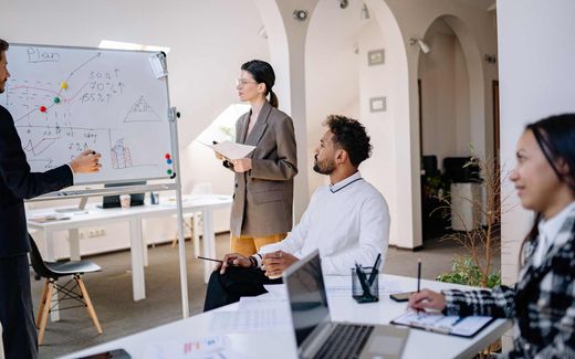 A team reviews charted figures and percentages on a whiteboard during an office planning session