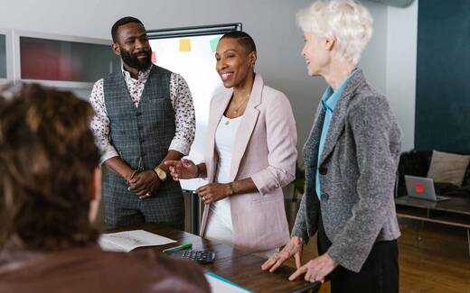 Four colleagues talk together around a conference table in a bright office