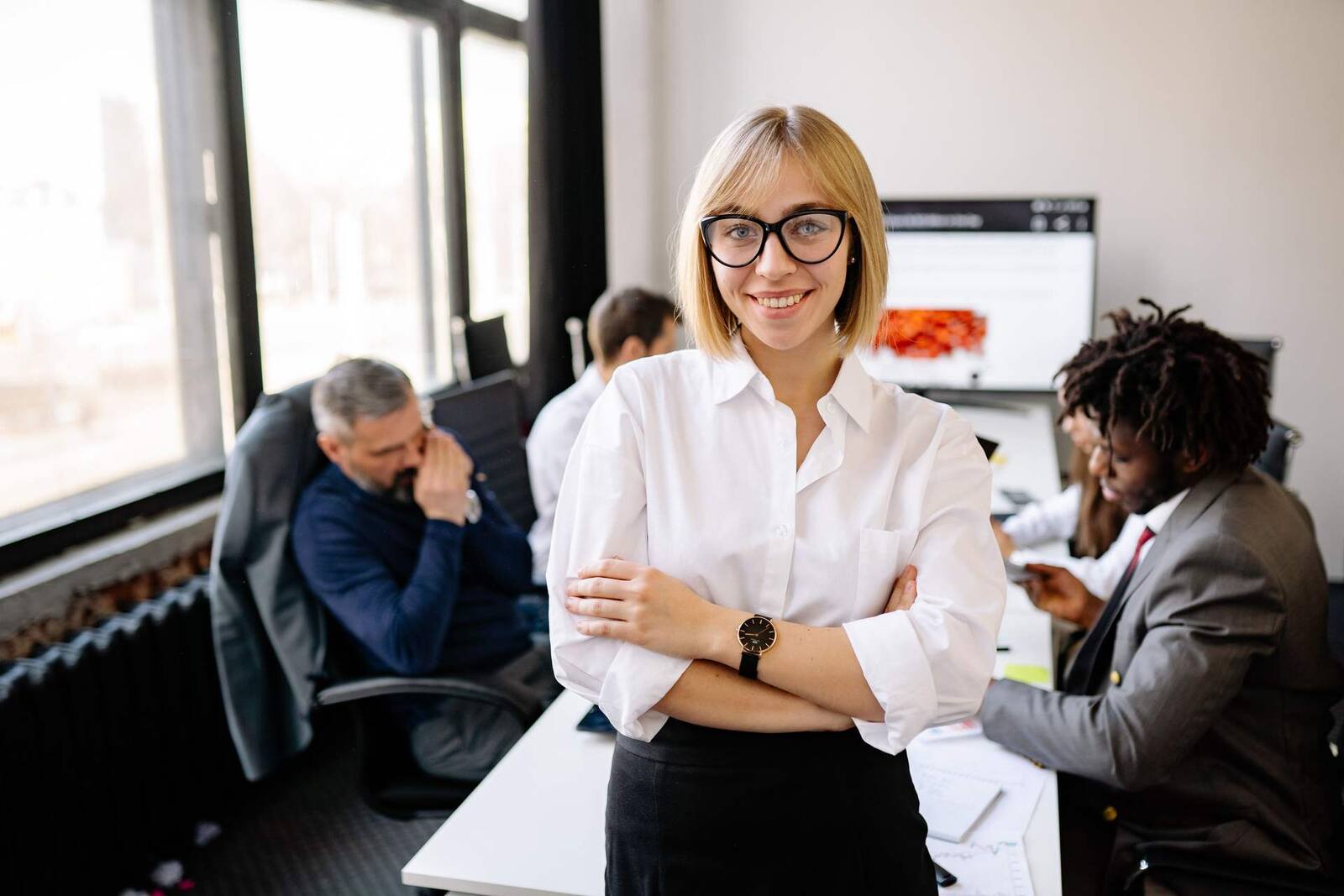 A business leader stands in an office with colleagues working in the background