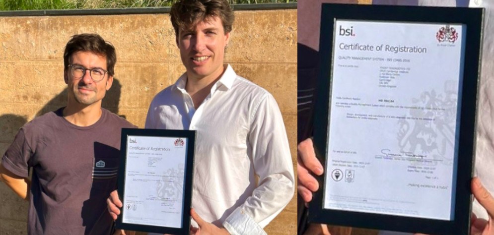 Two UpFront Diagnostics team members holding the company&rsquo;s framed BSI ISO 13485 certificate of registration, with a close-up of the certificate alongside