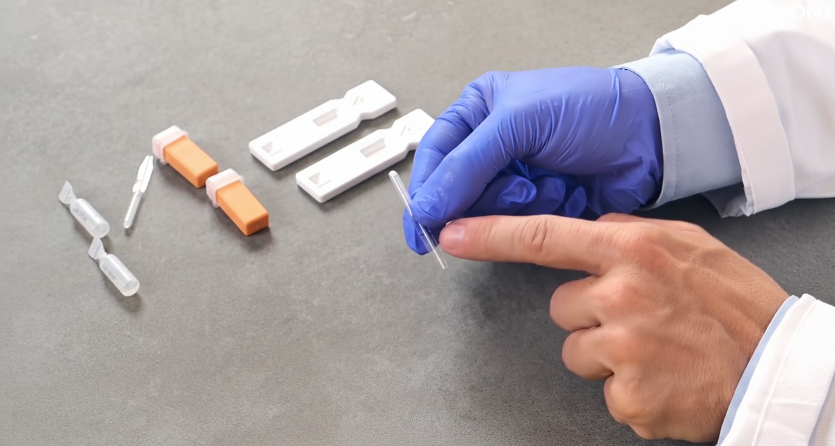 The LVOne kit laid out on a grey bench: two test cassettes, two lancets, buffer vials and a capillary tube held in a gloved hand