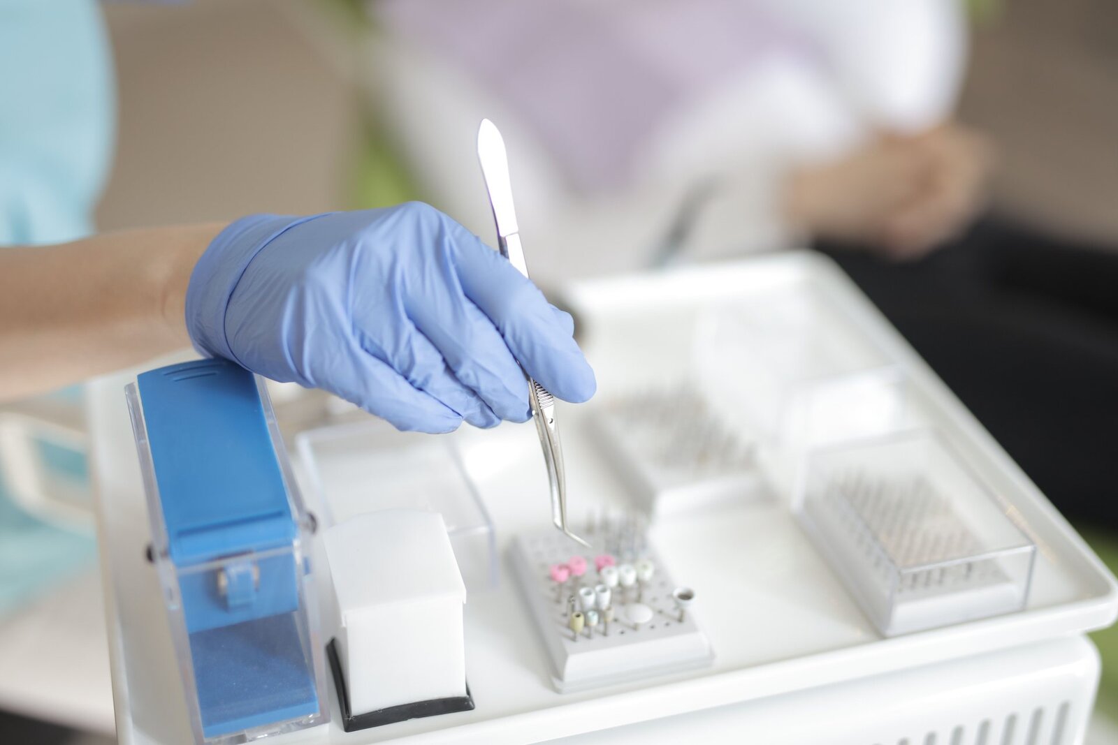 A gloved hand lifts forceps above a sterile surgical instrument tray