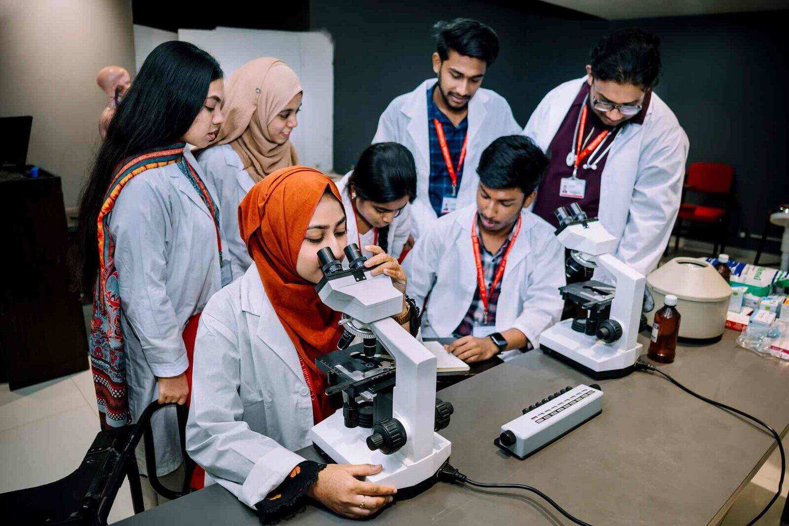 Two researchers in a bright teaching lab examine results together at a microscope station