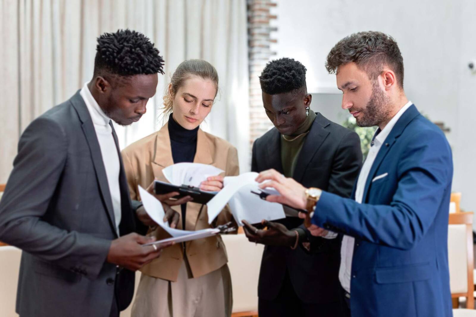 Four colleagues stand close together, marking up and comparing printed pages held between them