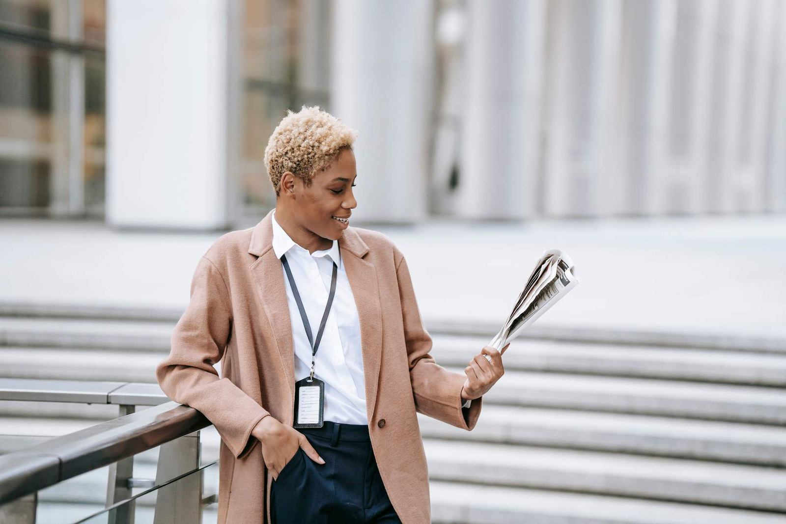A conference delegate wearing a lanyard reads a folded newspaper outside a venue