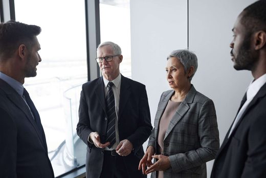Four business-attired attendees stand in animated conversation near a window in a bright, modern venue