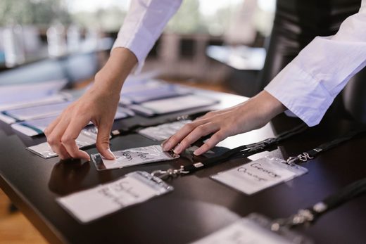 Two people’s hands arranging name badges and lanyards side by side on a dark conference registration table