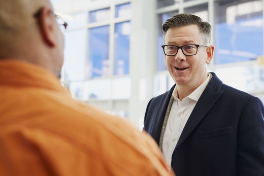 Two colleagues in close conversation in a bright atrium, one mid-sentence explaining something to the other