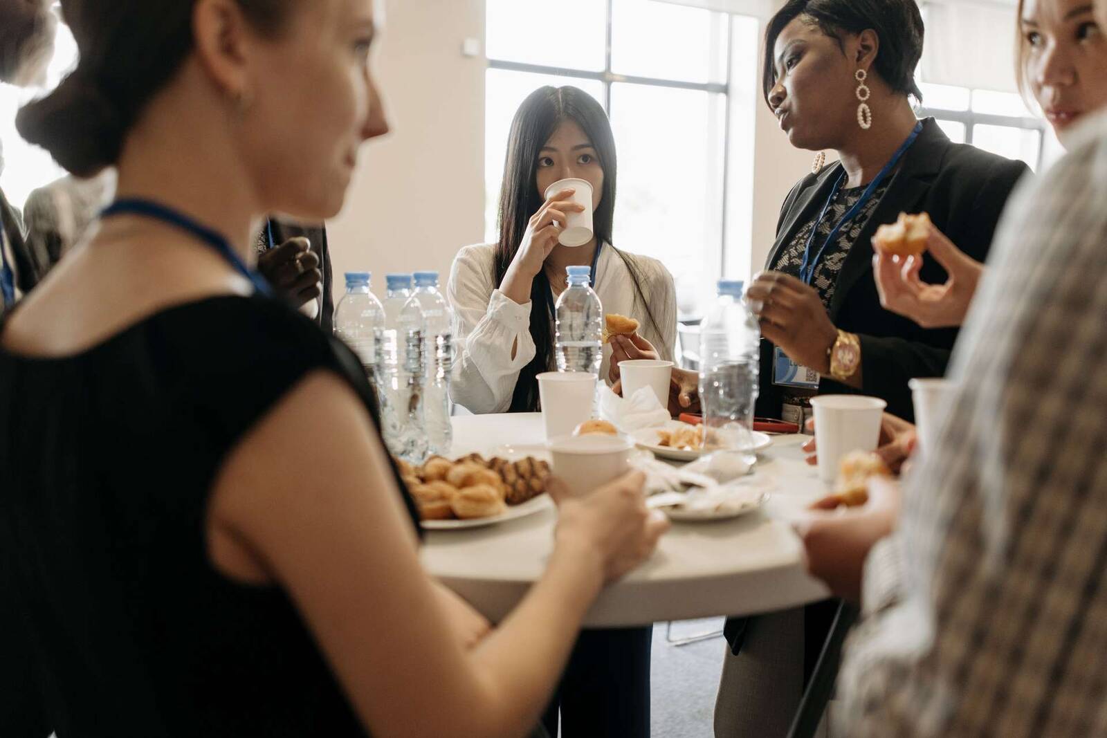Several delegates with conference lanyards stand together at a shared high table with coffee cups and pastries