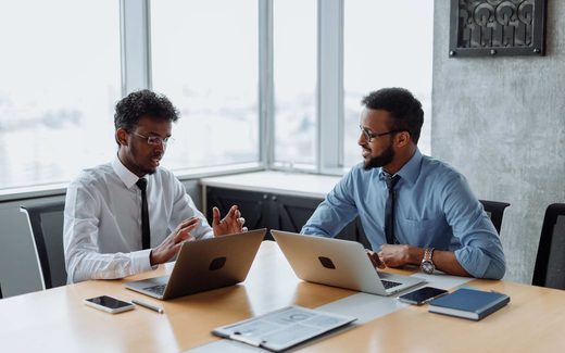 Two colleagues in business attire reviewing material together on laptops at a shared table