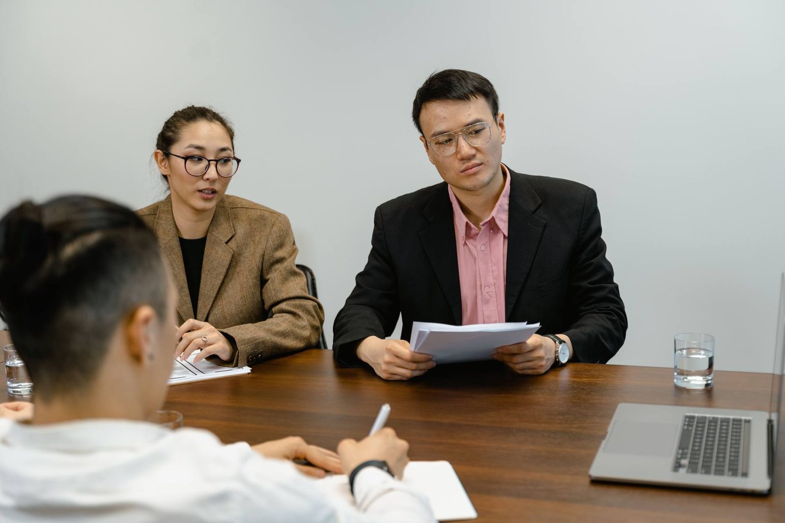 Two colleagues in a boardroom reviewing a document together while a third takes notes