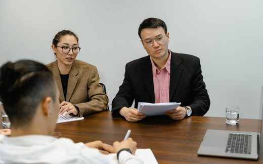 Two colleagues in a boardroom reviewing a document together while a third takes notes
