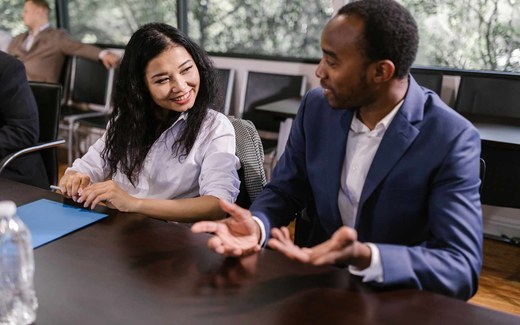 Two conference attendees smiling in conversation at a shared table during a break