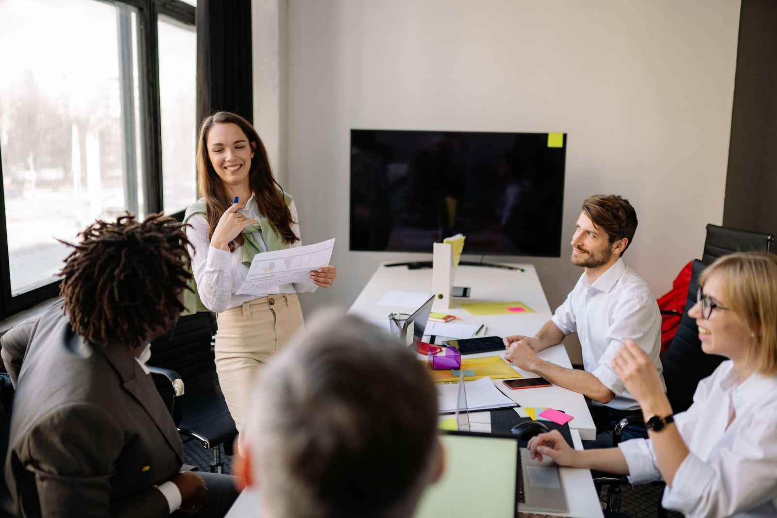 A presenter shares a printed chart with colleagues gathered around a bright meeting table