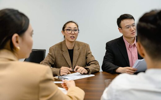 Colleagues in business attire talk through a point at a meeting table