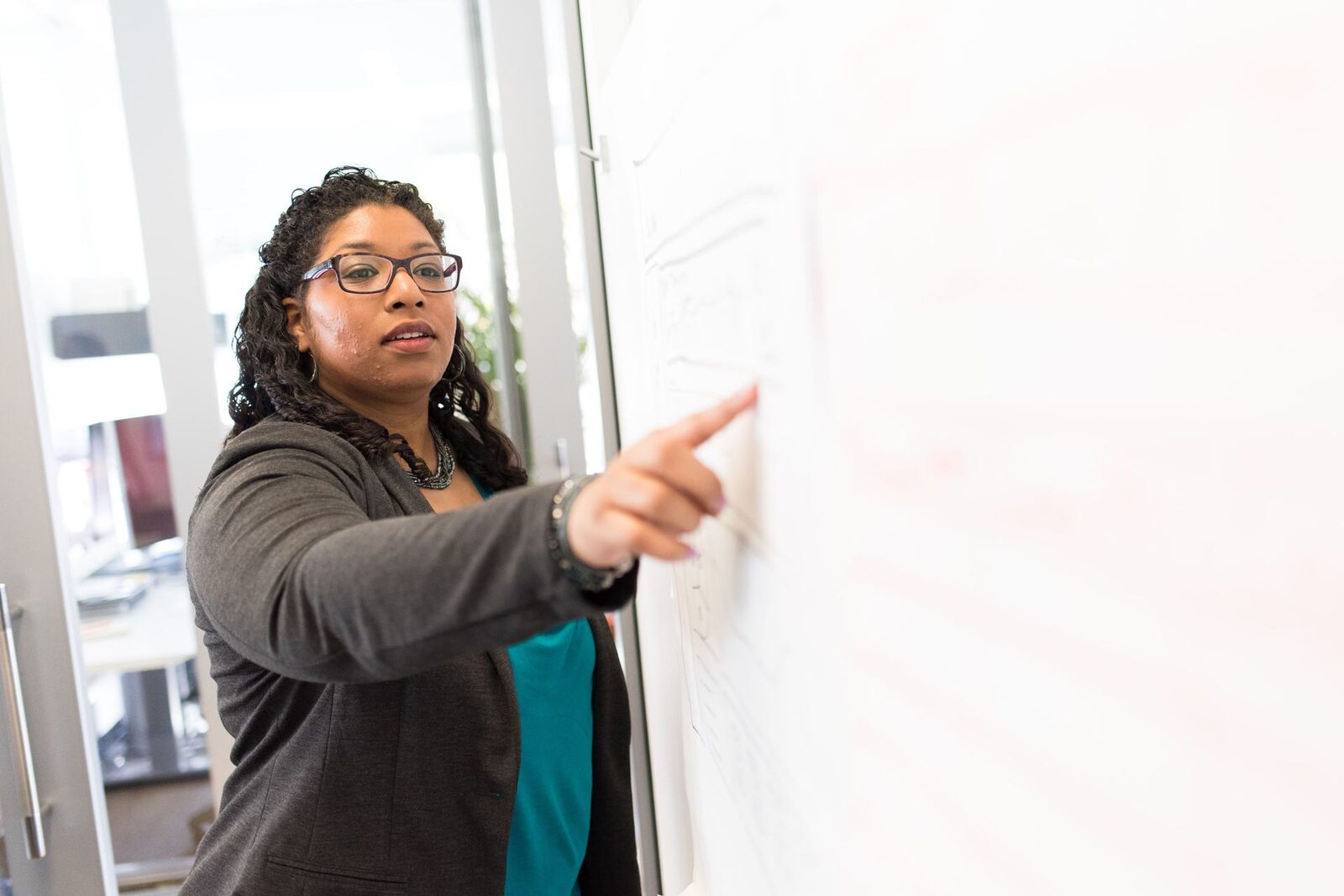 A presenter pointing to notes on a whiteboard while explaining a point to colleagues