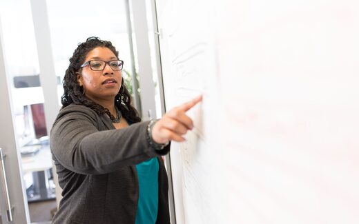 A presenter pointing to notes on a whiteboard while explaining a point to colleagues