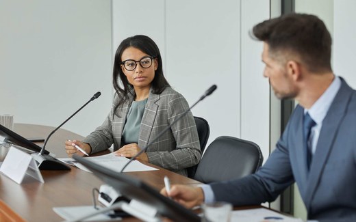 A panel of delegates seated at a conference table with microphones, listening attentively during a formal meeting
