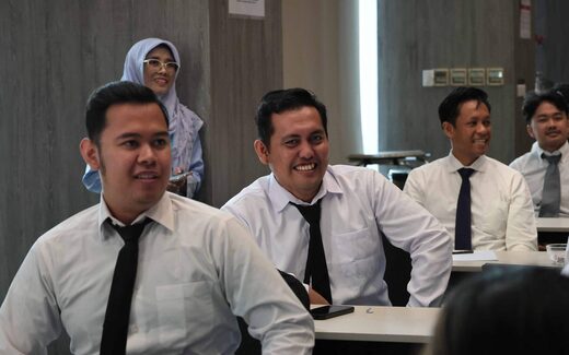 Attendees in business attire seated in a bright training room, smiling toward an unseen speaker