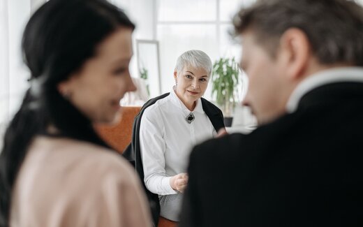 Colleagues in a bright meeting room pause mid-discussion around a small table