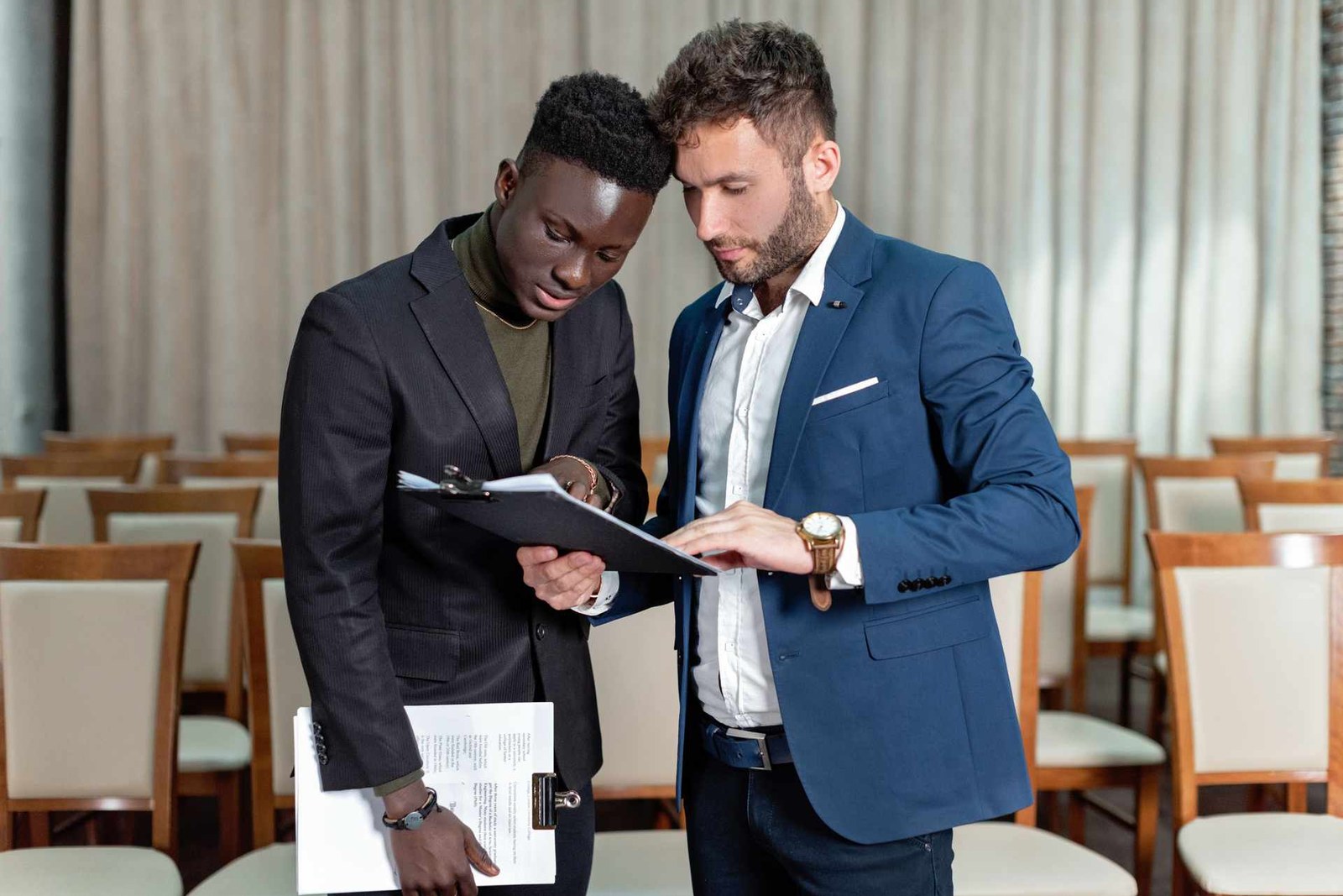 Two conference delegates reviewing a program agenda among rows of seminar chairs