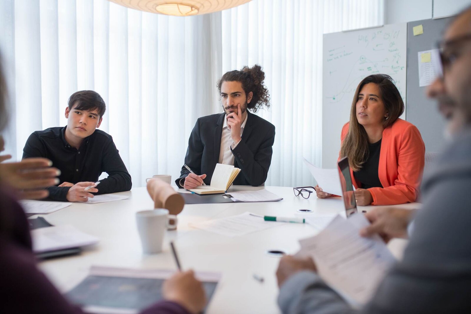 Three delegates listening and taking notes at a round table during a workshop-style training session
