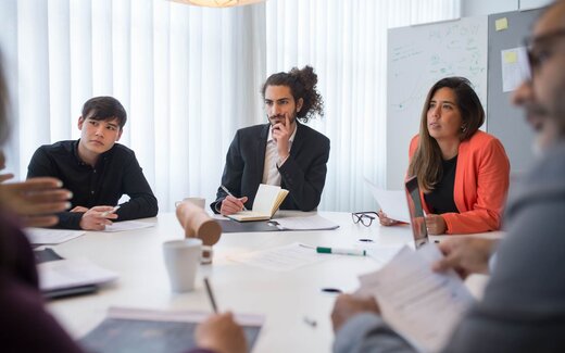 Three delegates listening and taking notes at a round table in a bright training room