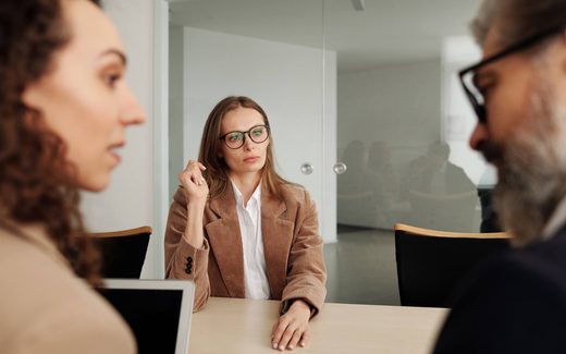 Three colleagues in discussion around a table in a glass-walled meeting room