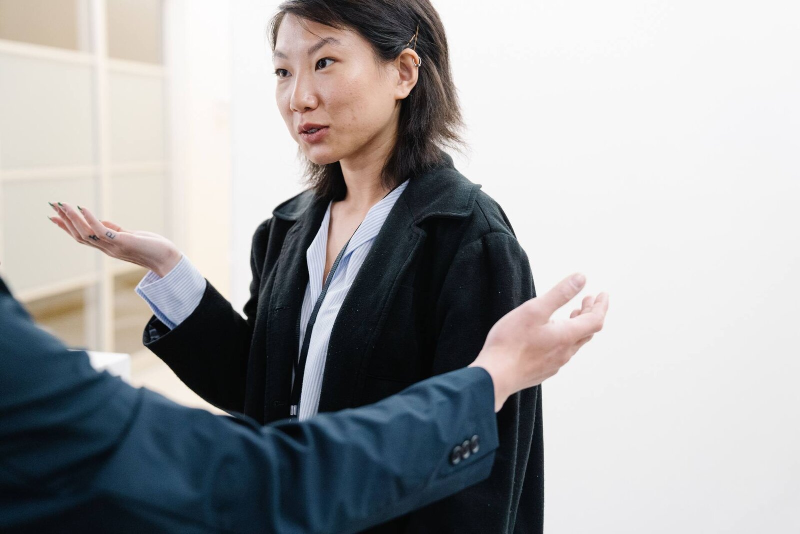 A businesswoman in a blazer, wearing a lanyard, gestures while speaking to colleagues