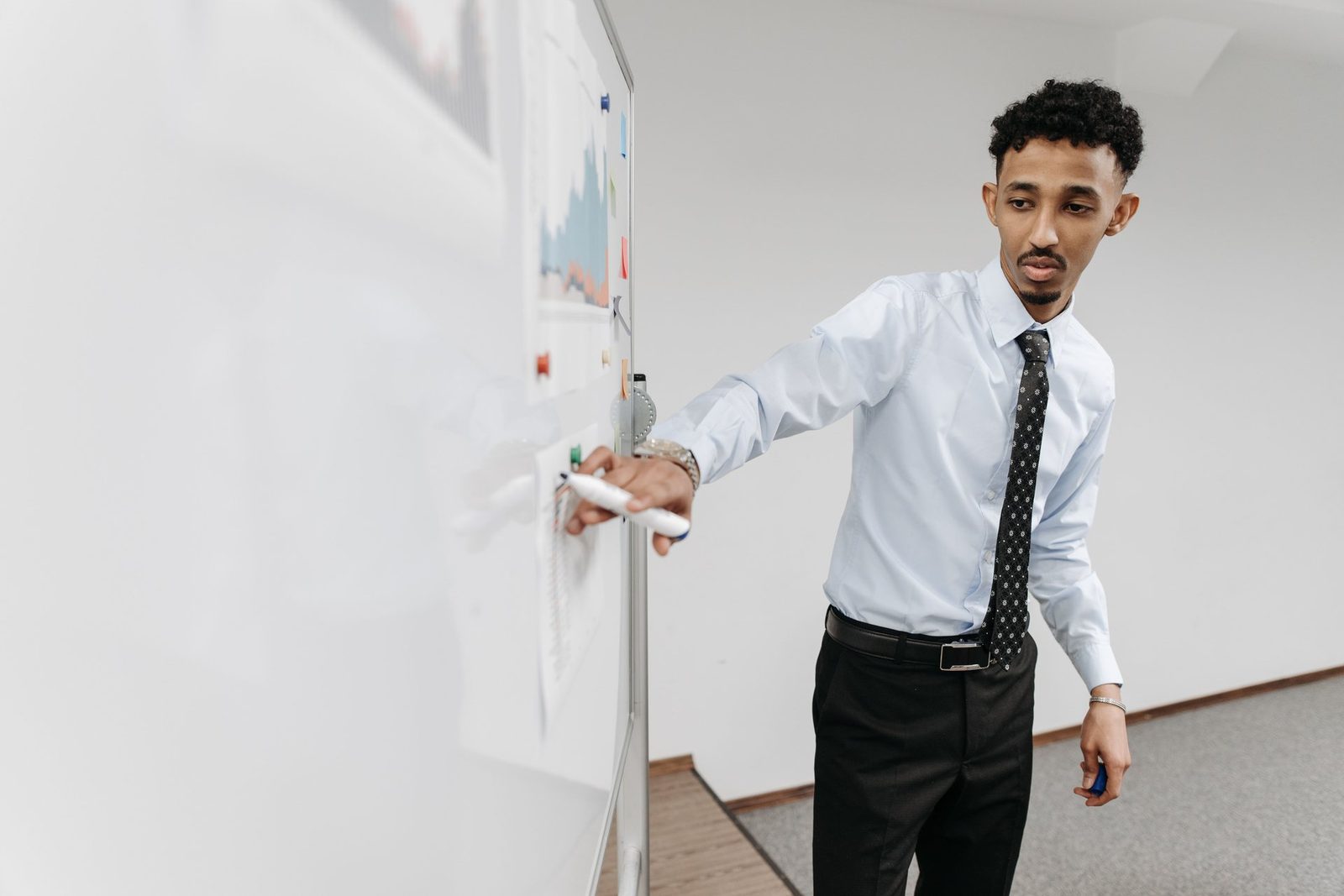 A presenter in a dress shirt and tie pointing to a chart drawn on a whiteboard
