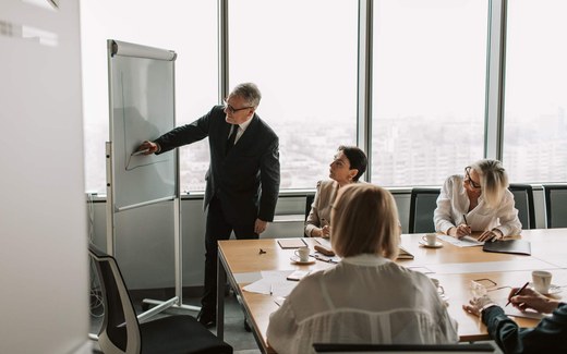 A presenter at a flipchart addressing colleagues seated at a table during a training session