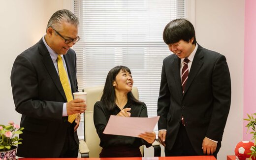 Three colleagues in business attire review a document together in an office