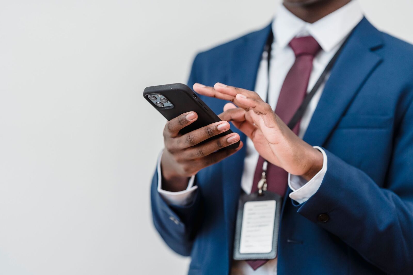 A conference delegate in a navy suit checks a smartphone, an event badge clipped to the lanyard around their neck