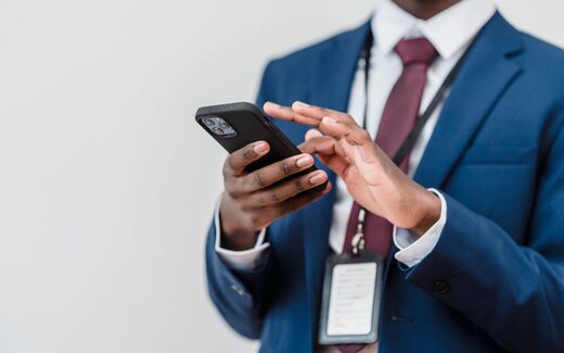 A conference delegate in a navy suit checks a smartphone, an event badge clipped to the lanyard around their neck