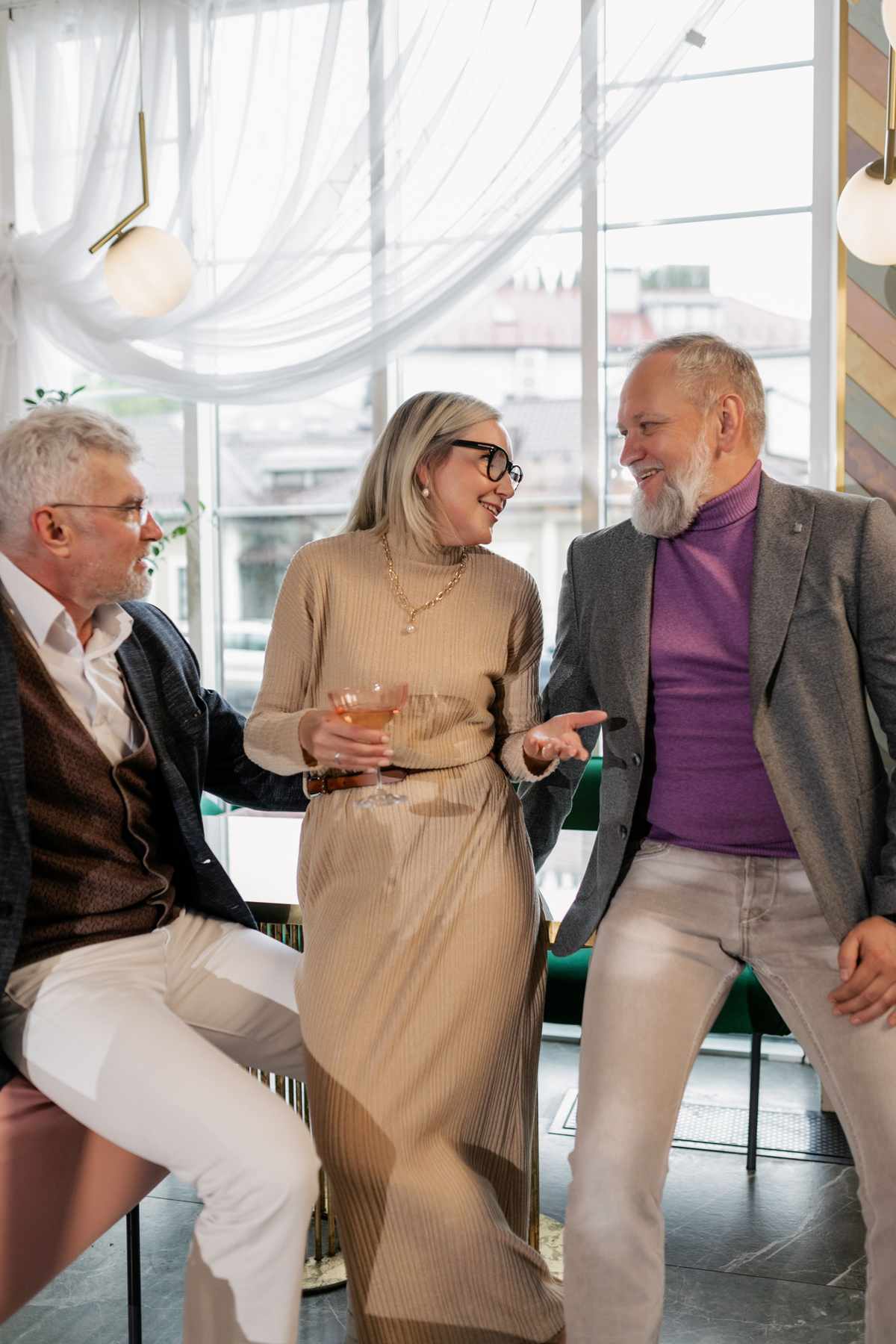 Three delegates laughing together over a drink at a bright conference reception